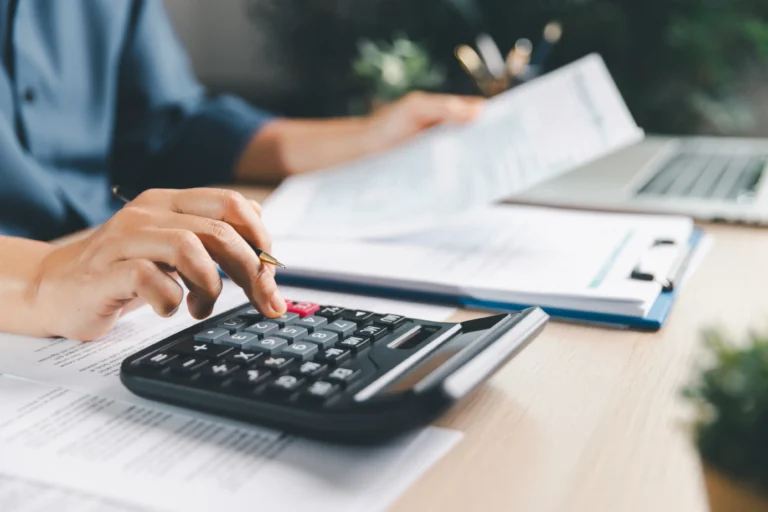 Person using a calculator while reviewing financial documents beside a laptop.